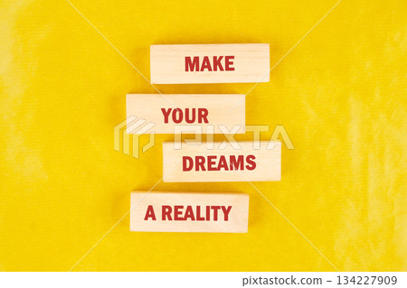 Bright yellow backdrop features wooden blocks arranged to convey an uplifting message about making dreams a reality. Perfect for motivating individuals to chase their aspirations Bright yellow backdrop features wooden blocks arranged to convey an uplifting message about making dreams a reality. Perfect for motivating individuals to chase their aspirations 134227909