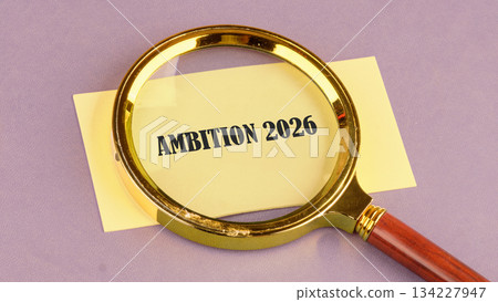 A golden magnifying glass rests on a yellow paper displaying the words ambition 2026, symbolizing a clear focus on future plans and dreams with determination and purpose A golden magnifying glass rests on a yellow paper displaying the words ambition 2026, symbolizing a clear focus on future plans and dreams with determination and purpose 134227947