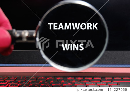 A hand holds a magnifying glass over bold text that reads teamwork wins, symbolizing the power and importance of collaboration in a modern workspace, illuminated by a glowing screen A hand holds a magnifying glass over bold text that reads teamwork wins, symbolizing the power and importance of collaboration in a modern workspace, illuminated by a glowing screen 134227966