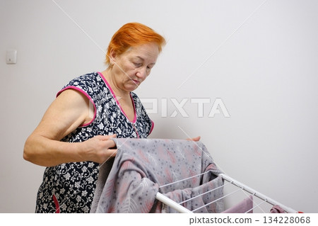 Beautiful woman hanging fresh clean laundry on drying rack at home Beautiful woman hanging fresh clean laundry on drying rack at home 134228068