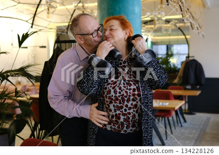 A man helps a woman put on her jacket and kisses her on the cheek. An adult couple, love, family, relationship, in a restaurant. A man helps a woman put on her jacket and kisses her on the cheek. An adult couple, love, family, relationship, in a restaurant. 134228126