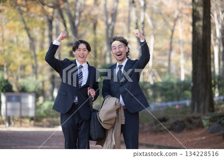 兩位面帶笑容的商人正在尋找工作或應屆畢業生，背景是秋冬季節。應屆畢業生和他們的老闆看向鏡頭，並擊掌慶祝。 134228516