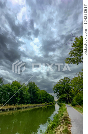 Serene rural scene, Winding pathway beside tranquil water under clouds 134228617
