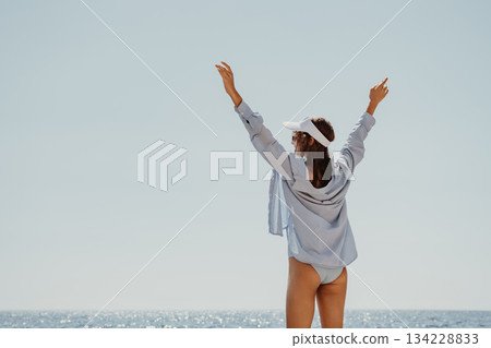 Woman Ocean Freedom, young woman raises arms celebrating summer joy by sparkling water, clear sky. 134228833
