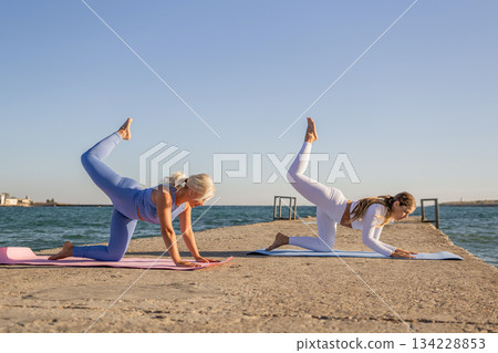 Yoga, Women, Beach: Two women practice yoga on a pier by the sea. Yoga, Women, Beach: Two women practice yoga on a pier by the sea. 134228853