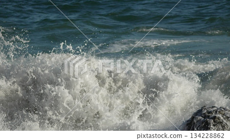 Ocean Waves Crashing. Powerful ocean waves collide with a shore rock, generating white foam and spray on a sunny day. Ocean Waves Crashing. Powerful ocean waves collide with a shore rock, generating white foam and spray on a sunny day. 134228862