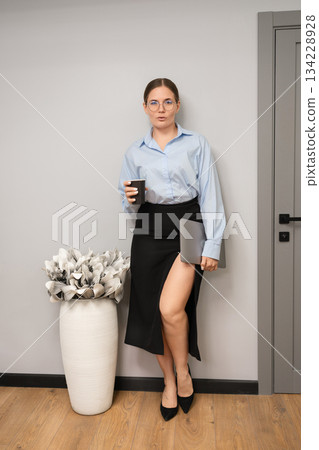 Businesswoman professional office worker holding laptop standing by a gray wall 134228928
