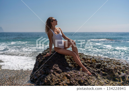 Woman beach summer enjoying sunny vacation sitting on ocean rock 134228941