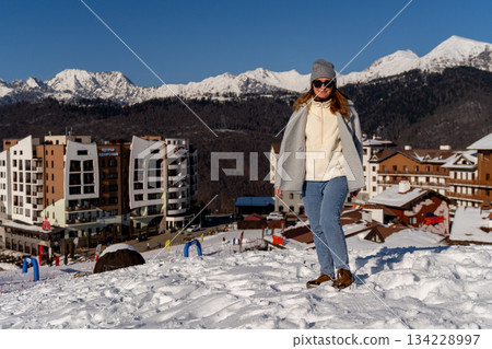 Woman Winter Caucasus Mountains Snow Resort Vacation: Scenic view of woman walking in snowy resort near Caucasus Mountains during winter vacation. 134228997