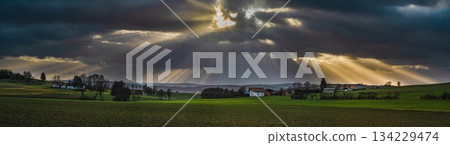 the sun's rays pierce the clouds over the agricultural field 134229474