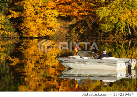 a motorboat and an autumn forest of red yellow and green autumn colors are reflected in the lake surface. a motorboat and an autumn forest of red yellow and green autumn colors are reflected in the lake surface. 134229494