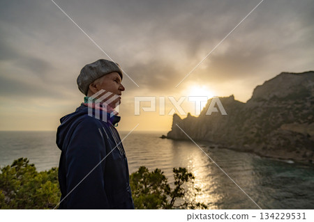 Senior woman sunset mountain looking over the vast sea and dramatic cliff landscape. 134229531
