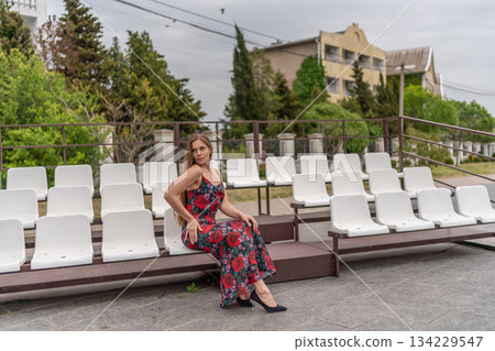 Woman dress stadium seats long floral gown sitting alone outdoors waiting area Woman dress stadium seats long floral gown sitting alone outdoors waiting area 134229547