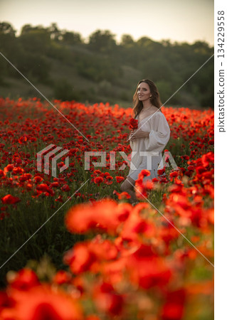 Woman in white dress walks through a poppy field. 134229558