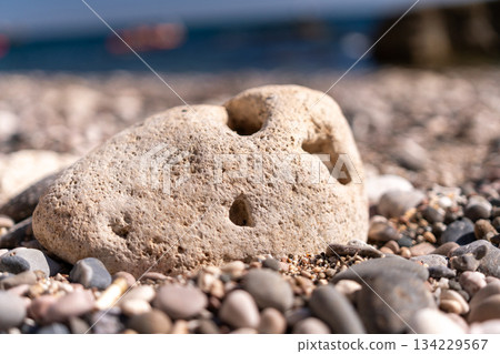 Stone beach ocean large porous stone rests on a pebble beach with blurred ocean background sunny day 134229567