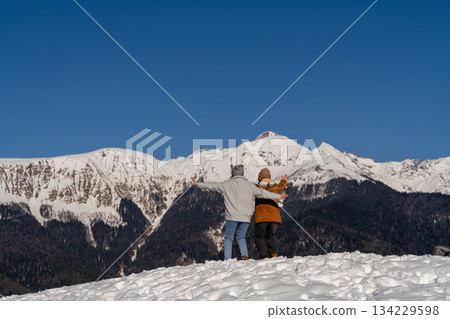 Mountains Couple Winter: Snowy peak view, embracing lovers enjoying scenic landscape, cold weather. Mountains Couple Winter: Snowy peak view, embracing lovers enjoying scenic landscape, cold weather. 134229598