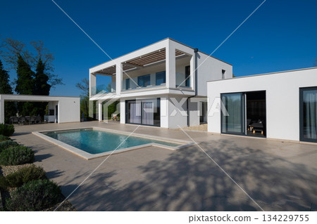 Modern luxury villa with pool, terrace, and minimalist architecture on a sunny day. Clean lines, large windows, and outdoor living spaces create a stylish contemporary home setting Modern luxury villa with pool, terrace, and minimalist architecture on a sunny day. Clean lines, large windows, and outdoor living spaces create a stylish contemporary home setting 134229755