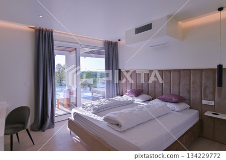 Bright, modern bedroom featuring a comfortable bed, sleek desk, and a large sliding glass door opening to a private balcony with stunning green landscape views, perfect for relaxation and serene Bright, modern bedroom featuring a comfortable bed, sleek desk, and a large sliding glass door opening to a private balcony with stunning green landscape views, perfect for relaxation and serene 134229772