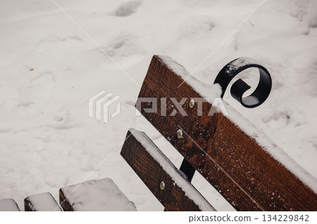 Snow-covered wooden park bench with decorative black metal elements against a thick white snow background Snow-covered wooden park bench with decorative black metal elements against a thick white snow background 134229842