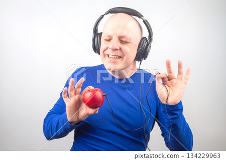 bald man with headphones listens to music through a red apple player bald man with headphones listens to music through a red apple player 134229963