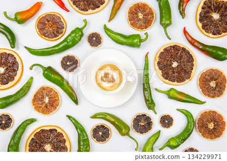 Cappuccino in a white cup centered among dried orange slices and green chili peppers 134229971