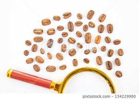 Scattered coffee beans with a golden magnifying glass on a white background 134229980