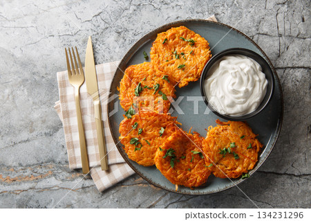 Sweet Potato Hash Browns with crispy edges and a buttery center served with sour cream closeup on the plate. Horizontal top view 134231296