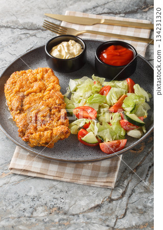 Sicilian breaded beef steak served with fresh salad and two sauces close-up on a plate. Vertical 134231320