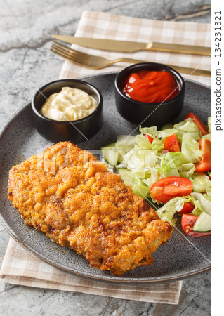 Tender Sicilian beef steak in a Parmesan and breadcrumb crust served with a fresh salad and two sauces close-up on a plate. Vertical 134231321