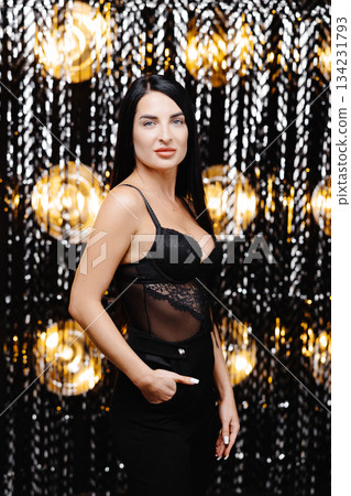 Young beautiful smiling brunette female in trendy evening clothes. Sexy carefree woman posing near shine wall in studio in a circle of light.Fashionable model with bright makeup Young beautiful smiling brunette female in trendy evening clothes. Sexy carefree woman posing near shine wall in studio in a circle of light.Fashionable model with bright makeup 134231793