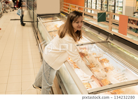 A woman opens the refrigerator door at a supermarket to select a French fries. 134232280