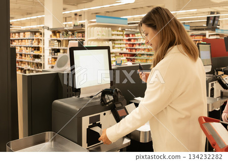 A woman pays with a card at a self-service checkout in a supermarket 134232282