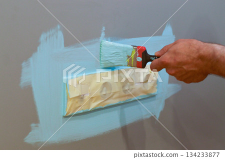 Home interior update involving painting around an electrical outlet with a brush, employing masking tape for protection, as part of a DIY project to maintain a tidy and safe space. 134233877