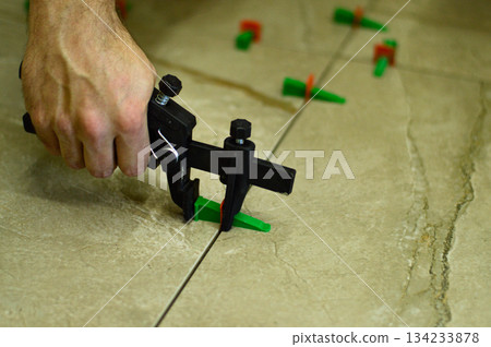 A professional tiler is carefully positioning a ceramic wall tile onto a layer of fresh adhesive, utilizing a lash tile leveling system for a perfectly flat surface. 134233878