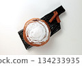 Round, delicious bun with cinnamon and powdered sugar on a black wooden board on a white background 134233935