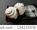 Fragrant cinnabons with cream on a black rectangular plate on a gray background 134233936