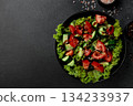 Vegetable salad of tomatoes, cucumbers, onions, lettuce dressed with aromatic dressing in a black plate on a gray background 134233937