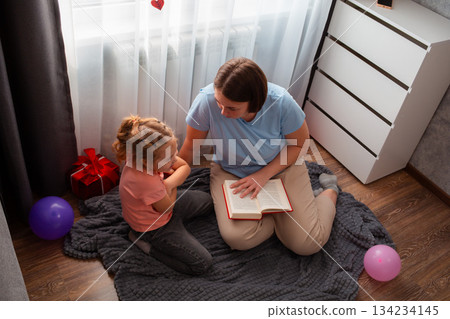 Top view young Caucasian woman speech therapist reads a book to a little girl. Teaching linguistics and language to a preschool child 134234145