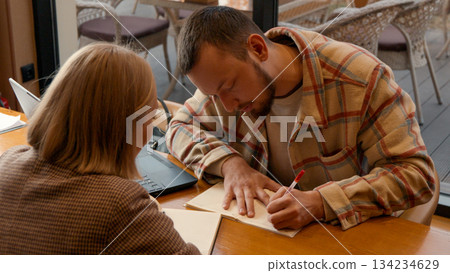 Two students focused on documents and making notes together in a cafe Two students focused on documents and making notes together in a cafe 134234629