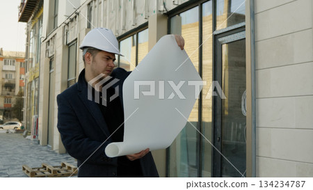 Architect with blueprints outside a modern building, serious expression Architect with blueprints outside a modern building, serious expression 134234787