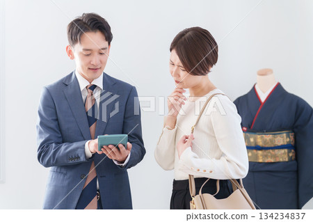 一位男性和服銷售員和一位正在估價的女性顧客 一位男性和服銷售員和一位正在估價的女性顧客 134234837