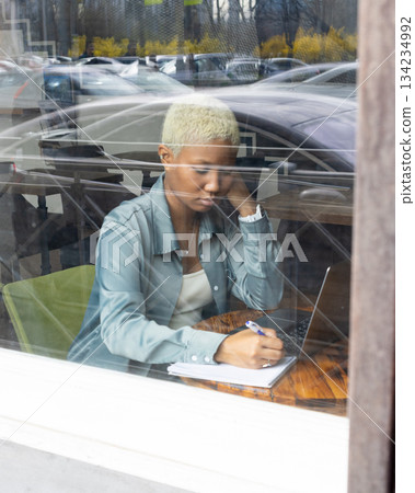 African American woman with short blond hair sits at table and types on laptop. 134234992