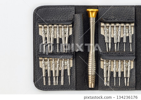A black leather case holds a set of miniature screwdrivers. The set includes a handle with a gold top and interchangeable bits. 134236176