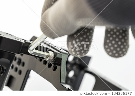 A gloved hand tightens a screw on a black metal frame.  An Allen wrench is in use, and the background is a clean, bright white. 134236177