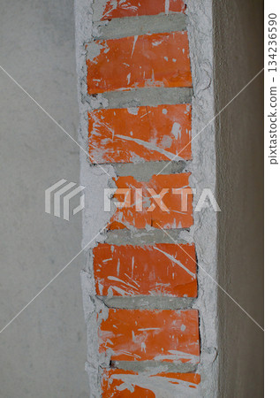 Close-up of a damaged red brick wall with large sections of gray render cracked and peeling off, exposing the bricks underneath. 134236590