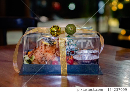 A roasted chicken arranged in a festive transparent gift box with ribbon and ornaments. Ideal for Christmas promotions, seasonal menus, and winter celebration visuals 134237099