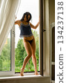 Sensual attractive brunette woman posing over the window wearing sexy lingerie, looking at camera. 134237138