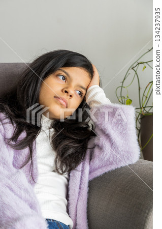 A young girl is sitting on a couch with her head on her hand A young girl is sitting on a couch with her head on her hand 134237935