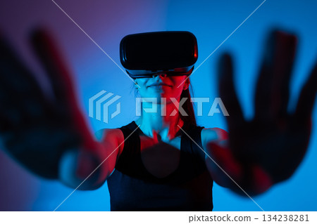 Woman using VR headset with extended hands in neon lighting while engaging with virtual reality interface 134238281