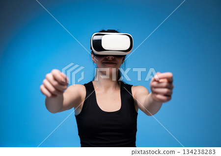 Smiling woman using VR headset with extended arms interacting in immersive digital blue environment Smiling woman using VR headset with extended arms interacting in immersive digital blue environment 134238283
